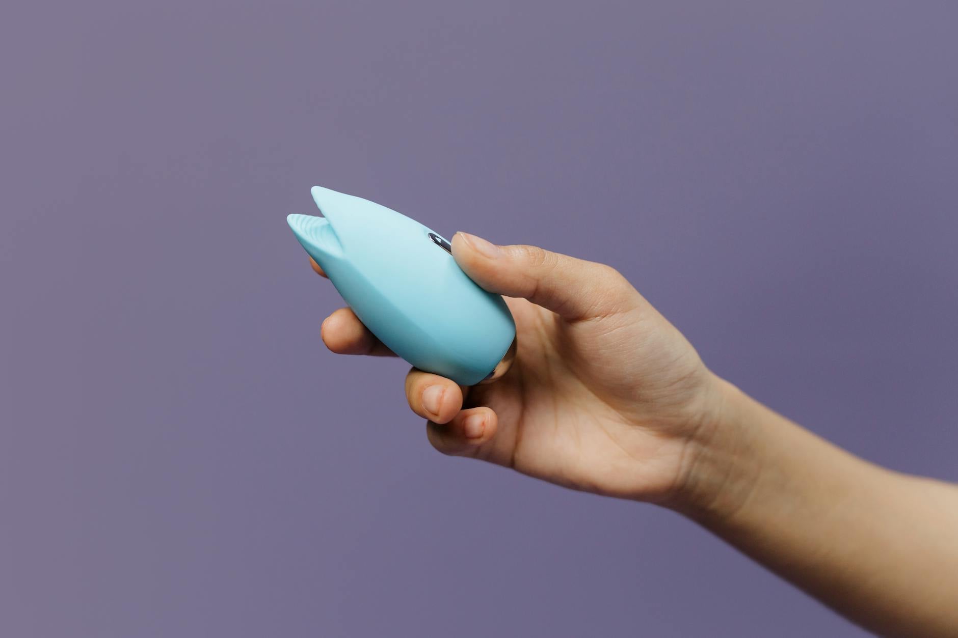 A blue silicone vibrator held in hand against a purple background, symbolizing gentle self-pleasure