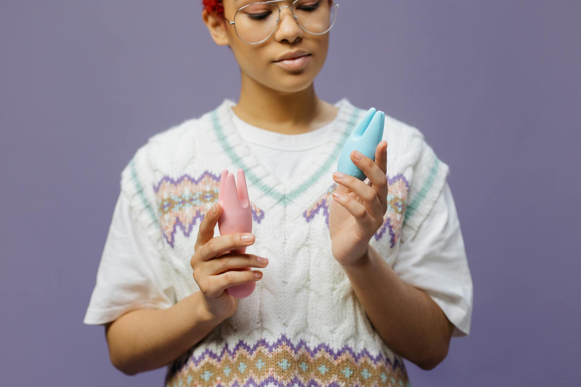 Woman holding contemplative expression while exploring clitoral vibrators with blue and pink silicone toys.