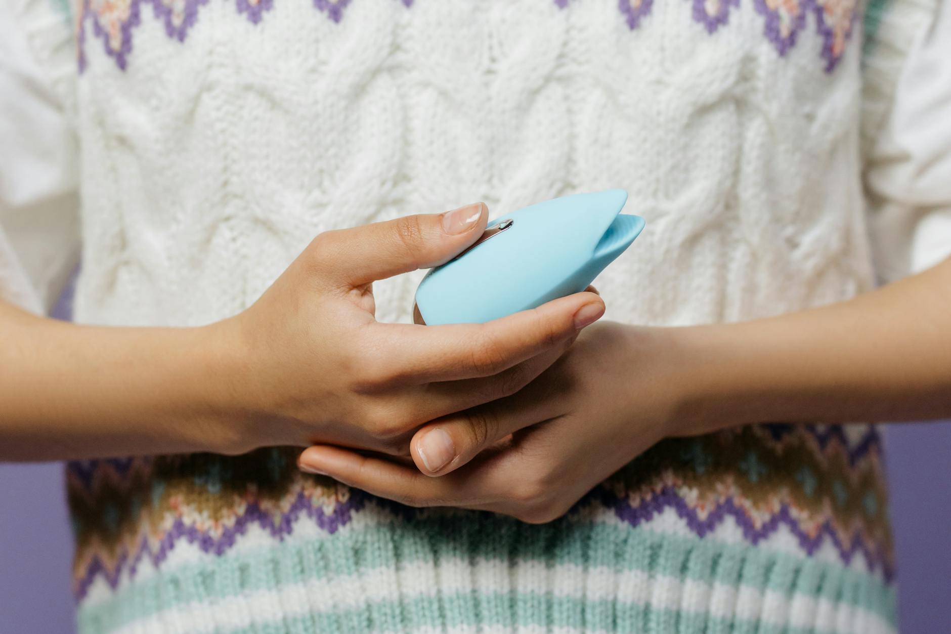 Close-up of hands holding a blue personal massager against a knitted sweater while sitting peacefully
